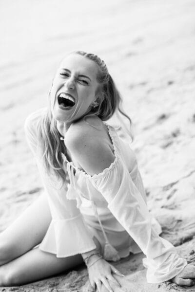 risingqueen- Lachende Frau am Sandstrand, die ihre persönliche Marke präsentiert.