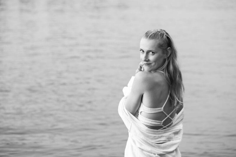 risingqueen- Eine Frau blickt auf einem Schwarz-Weiß-Foto über die Schulter in der Nähe eines Gewässers und verkörpert die Essenz einer persönlichen Marke.